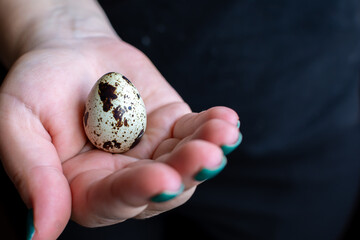 Girl holding a quail egg in the palm of her hand, dark background