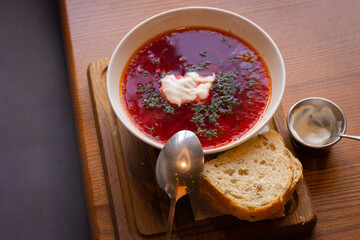 Ukrainian borsht with bread on wooden table. Red soup with cream and bread. Ukrainian traditional food. Homemade borscht. Tomato soup for dinner. Ukrainian cuisine. 