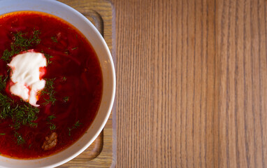 Ukrainian borsht on wooden table with copy space. Red soup with cream and parsley. Ukrainian traditional food. Homemade borscht. Tomato soup for dinner. Ukrainian cuisine. 