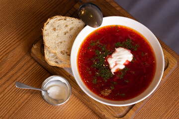 Ukrainian borsht with bread on wooden table. Red soup with cream and bread. Ukrainian traditional food. Homemade borscht. Tomato soup for dinner. Ukrainian cuisine. 