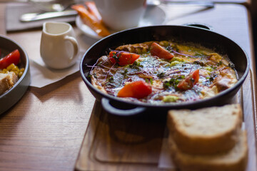 Fried eggs with tomato and ham in pan. Served breakfast table. Omelette with tomato and bread. Spanish tortilla. Eggs with pesto and vegetables. Ready to eat food. Healthy dinner. 