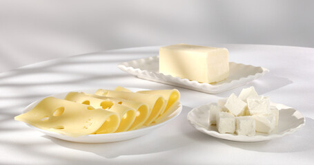 dairy products on a light background. cheese and butter on white plates. feta cheese close-up. slices of gouda cheese. piece of butter in the background.