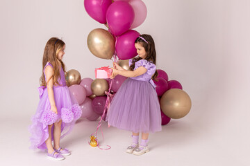 Obraz na płótnie Canvas Birthday celebration concept, little princess in lilac dresses, cheerful preschool girl party, two girls with balloons on the background, copy space