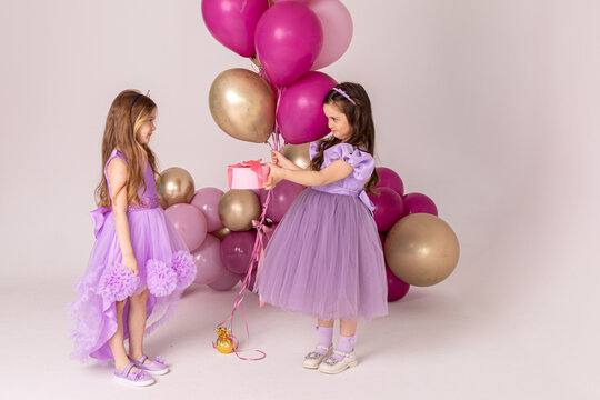 Birthday celebration concept, little princess in lilac dresses, cheerful preschool girl party, two girls with balloons on the background, copy space