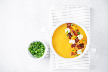 Potato carrot soup with fried bacon slices in a bowl