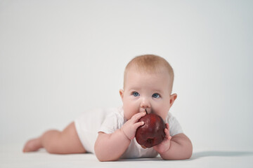 Baby 7 months old eats a red apple, photo on a light background
