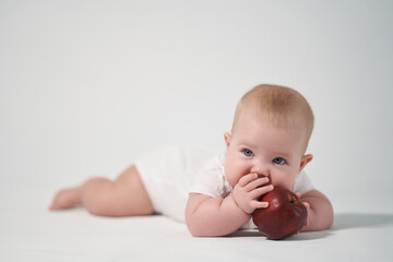 Baby 7 months old eats a red apple, photo on a light background
