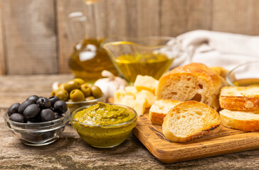 Ciabattas, olive oil in a bowl with olives, herbs, spices, garlic, pesto, parmesan and ciabatta bread on a texture background.Banner. Healthy food concept.Delicacy. Mediterranean Kitchen. Copy space.