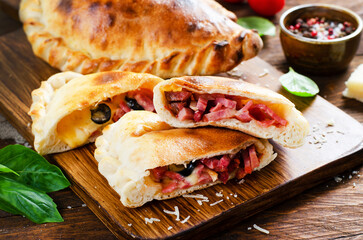 Delicious Pizza Calzone, Italian Pizza Stuffed with Ham and Cheese with Tomatoes and Fresh Basil on Wooden Background