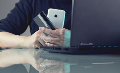 A man in front of his laptop holding a smartphone and a credit card. Secure payments online. Online shopping and e-commerce concept.