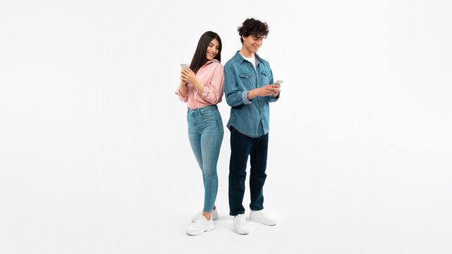 Young Couple Using Mobile Phones Texting Standing On White Background