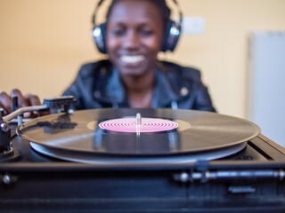 young woman wearing a leather jacket using headphones while playing a vinyl record on a vintage turntable