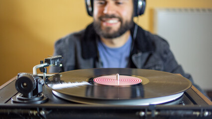 Young man using headphones while playing a vinyl record on a vintage turntable