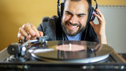 Young man using headphones while playing a vinyl record on a vintage turntable