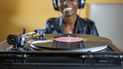 Fototapeta na wymiar young woman wearing a leather jacket using headphones while playing a vinyl record on a vintage turntable