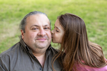 Fototapeta premium Daughter kisses her father in the park. Father's Day. Happy daughter kisses her father. Close-up. Copyspace.