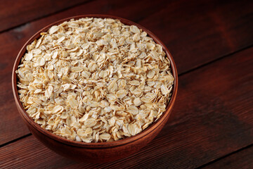 Oat flakes in a clay bowl on a wooden background. Dry rolled oatmeal on wooden boards. Copy space
