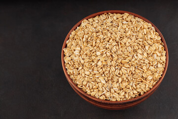 Oat flakes in clay bowl on a dark background. Raw oatmeal for healthy nutrition. Top view. Copy space