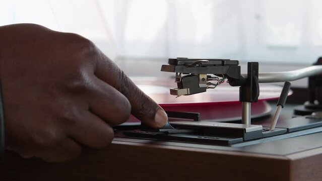 Detail of a female hand placing the needle on the track of a red vinyl record. Vintage turntable