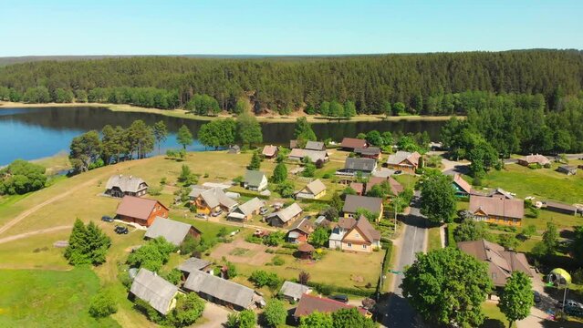 Aerial view Beautiful countryside Lithuanian houses in Paluse village by Lusiai lake coastline by forest in sunny day outdoors. Baltics lifestyle and culture