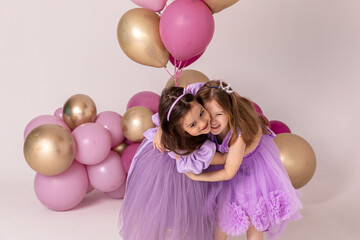 Birthday celebration concept, little princess in lilac dresses, cheerful preschool girl party, two girls with balloons on the background, copy space