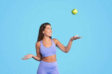 Smiling young european slim woman athlete brunette in sportswear tossing green apple, has fun