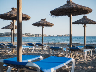 Straw umbrellas and blue sunbeds in a mediterranean beach