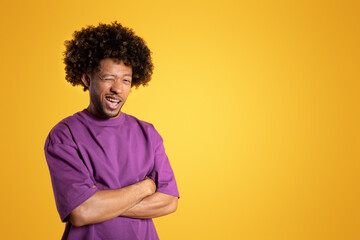 Fototapeta na wymiar Positive confident mature black curly guy in purple t-shirt with crossed arms on chest