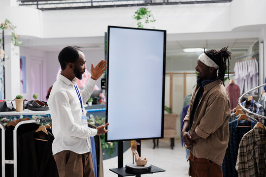 Mall employee advertising shoes brand to buyer, showcasing brand new collection on empty digital whiteboard mock up. Store assistant showing stiletto to customer on interactive display