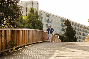 Happy european senior man in casual enjoys walking, jogging or training with dog, have fun, outdoor