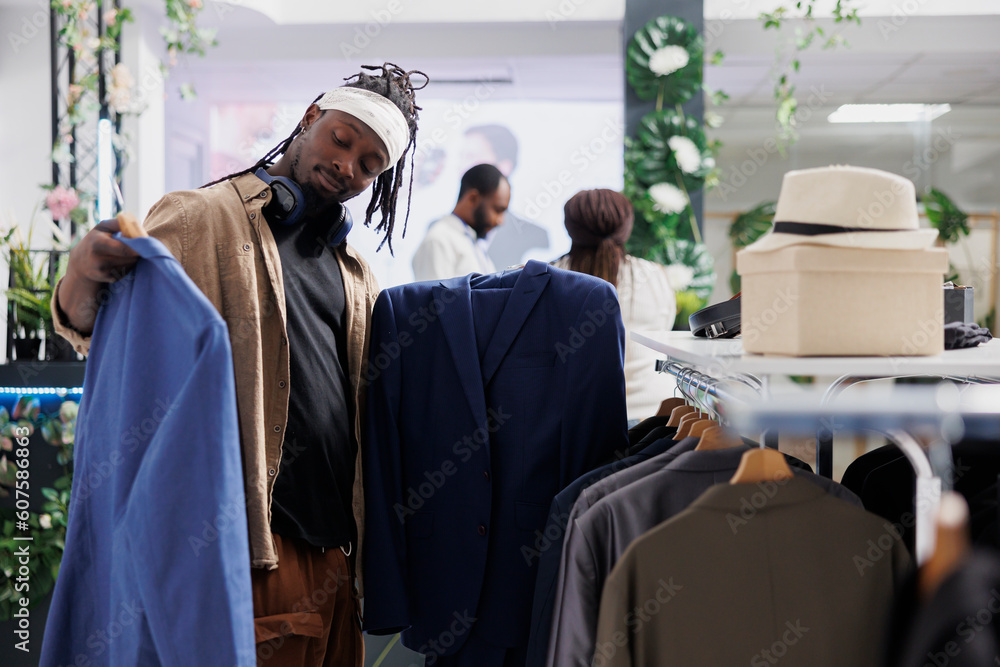 Wall mural buyer deciding between two jackets while choosing formal wear in clothing store. african american ma