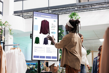 Customer using touch display shopping for fashion items in clothing store, interactive board....