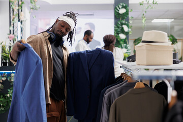 Buyer deciding between two jackets while choosing formal wear in clothing store. African american...