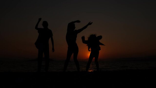 Silhouette of a dancing mother with her daughters. Crazy daughters dance with their mother against the backdrop of a sea sunset.