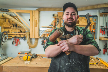 Portrait of confident carpenter holding hammer and chisel in woodworking studio. High quality photo