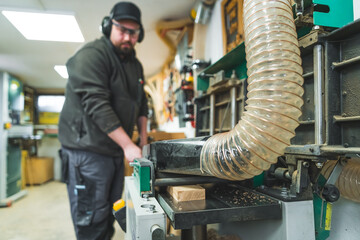 Carpenter with protective glasses and headset near sawdust extractor at workshop. High quality photo
