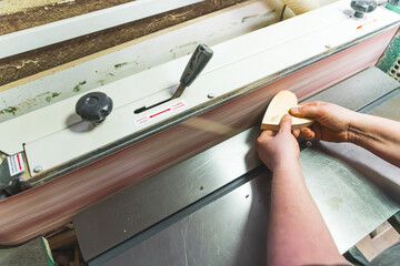 carpenter griding a heart shaped wooden piece by using a grinding machine in a workshop. High...