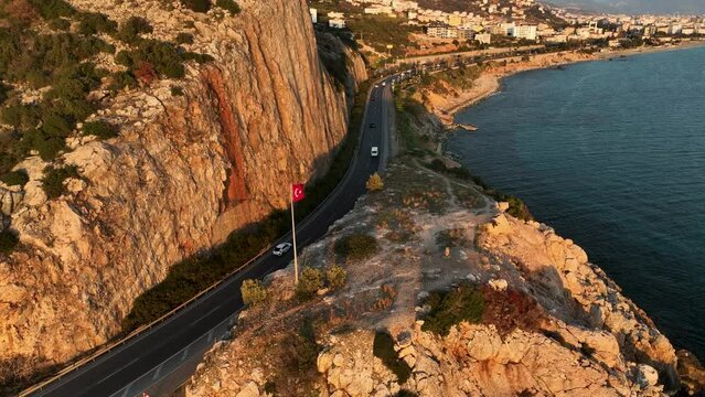 Flying drone over the coastline of the city Alanya overlooking the road, rocky shoreline with vegetation and rocks and clear sea with light foamy waves