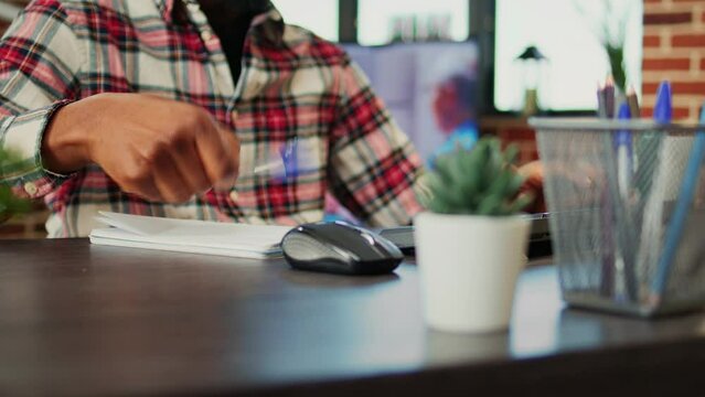 Employee working from home cross referencing information, transcribing data from computer to notebook. Teleworker remotely working in warm cozy stylish home, typing and writing, close up