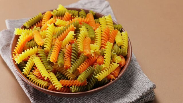 Colorful italian raw pasta on a linen napkin. Tricolor fusilli pasta on a clay plate. Panning camera shot