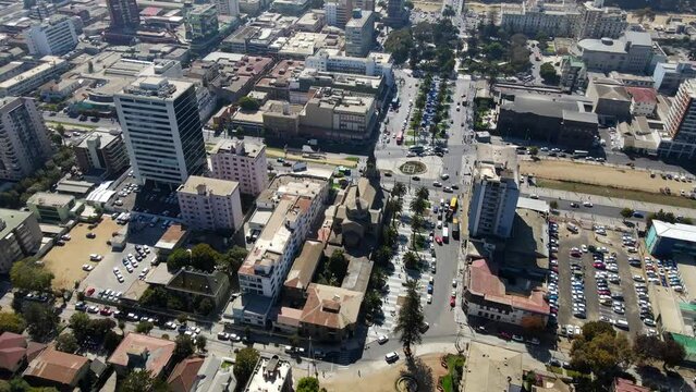 Aerial shot drone flies high over tree lined main street heading toward central park in roundabout