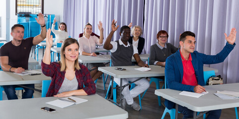 Portrait of multinational student group with hands raised during lesson in auditorium