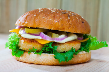 Tasty grilled burger with chicken nuggets, cheese, lettuce, onion, pickled cucumbers