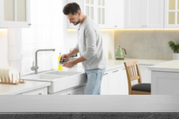 Man doing washing up in kitchen, focus on empty grey stone table