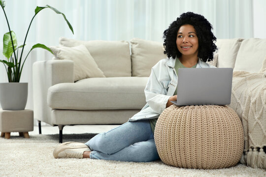 Happy young woman using laptop on pouf at home. Space for text