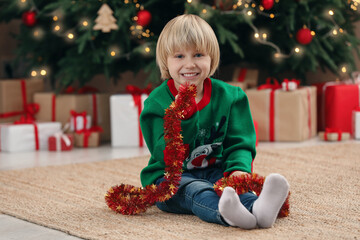 Little child with bright tinsel on floor at home. Christmas decoration