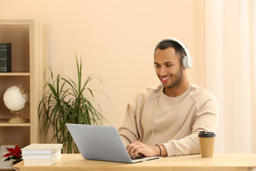 Smiling African American man in headphones working on laptop at wooden table indoors