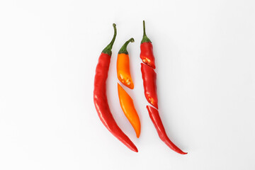 Whole and cut different hot chili peppers on white background, flat lay