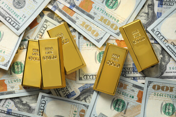 Many shiny gold bars on dollar banknotes, flat lay