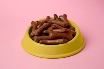 Yellow bowl with bone shaped dog cookies on pink background, closeup